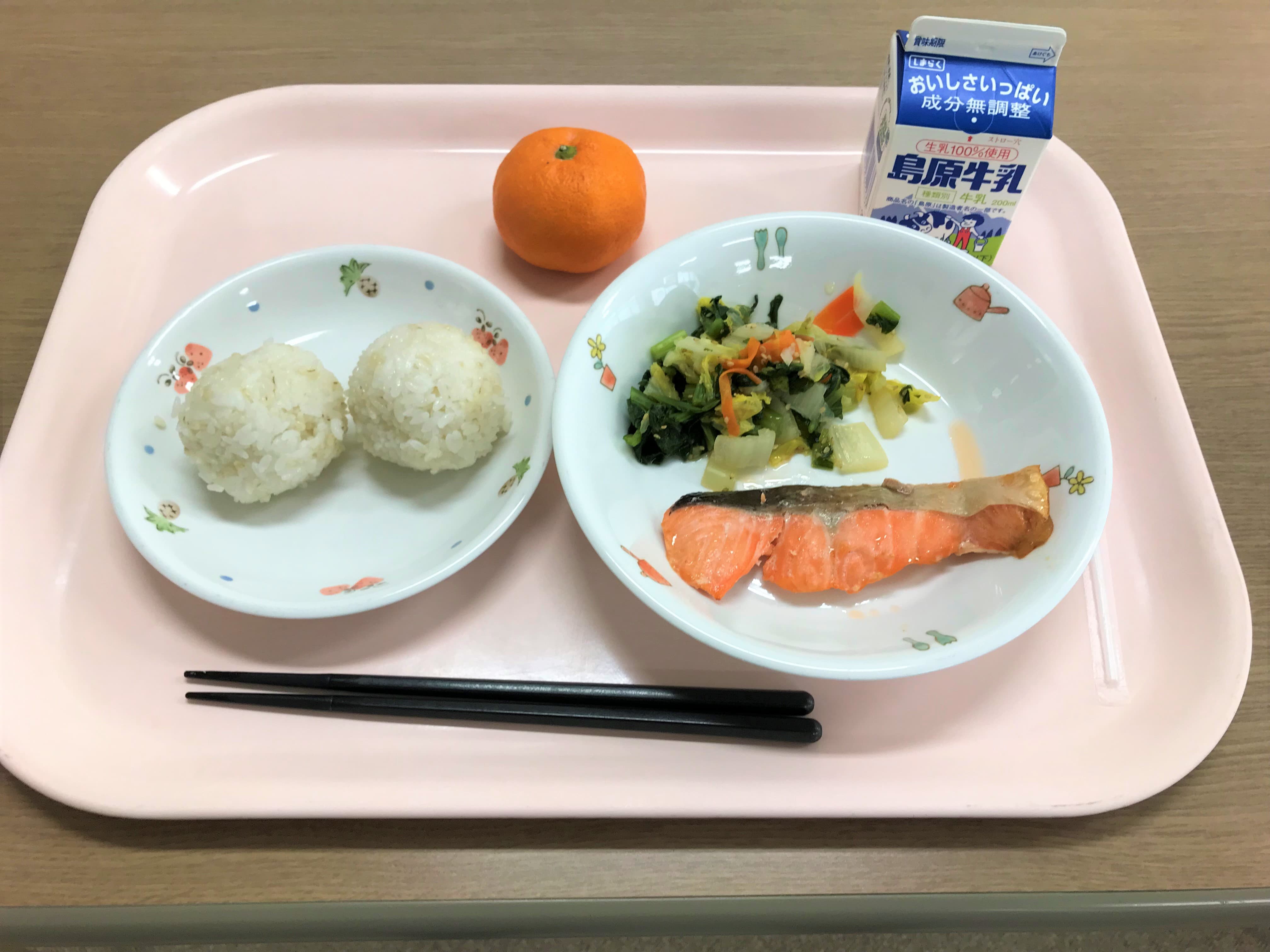 学校給食が始まった明治時代の給食の写真（おにぎり、焼き鮭、青菜の浅漬、みかん、牛乳）