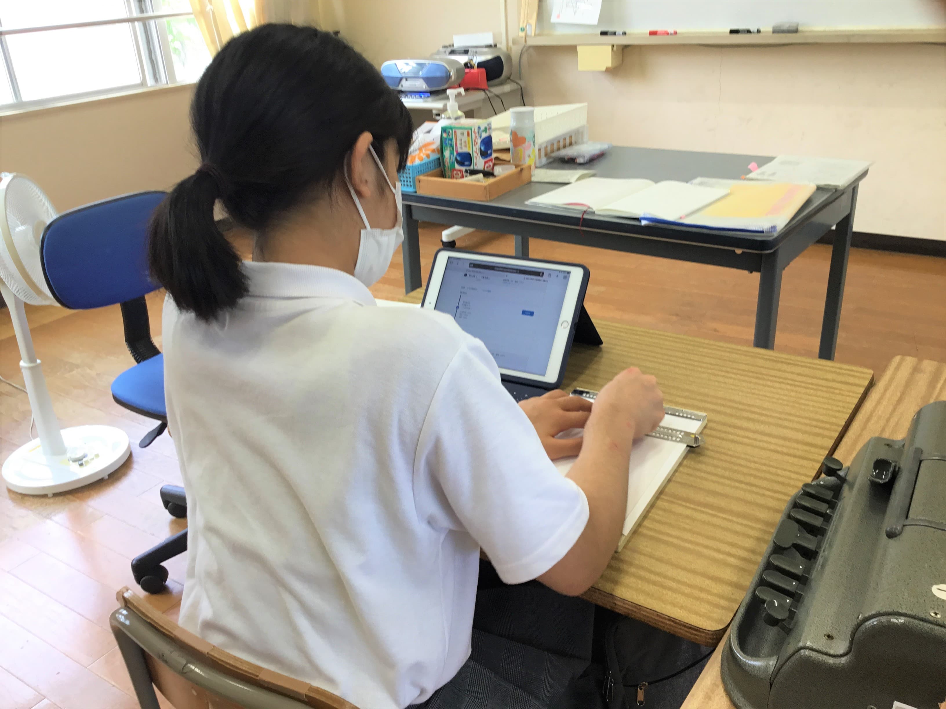中学部２年の生徒が、職場体験学習に行くときのバスの時刻を、タブレット端末で調べて、点字器で記録をしている様子